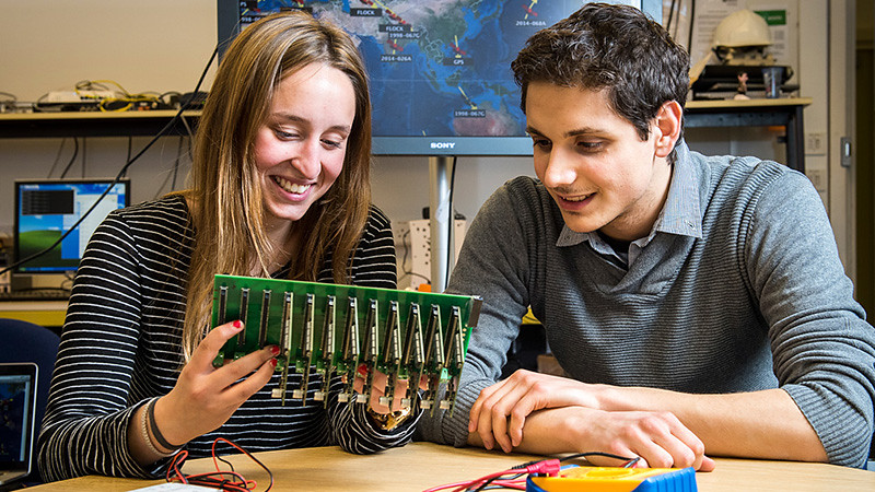 两个学生坐在实验室里看着一块电路板