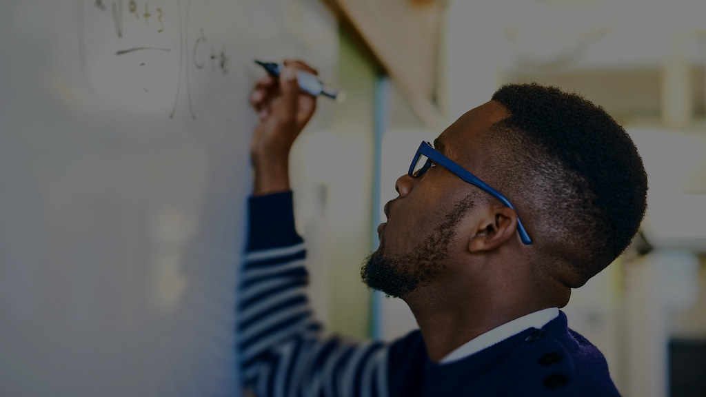 Photo of a male student writing mathematical calculations on a whiteboard.