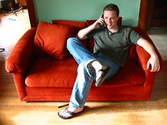 A young man lounging on a couch, talking on the phone.