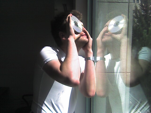 A photo of a man looking at the sun by covering one eye, and placing a compact disc over the other.