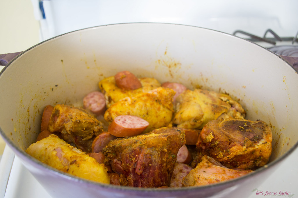 Next step in making Dominican stew is drizzle olive oil in a large dutch oven and sear the pork bones and chicken on both sides until outside is golden brown. Then add sausage and sear on both sides.