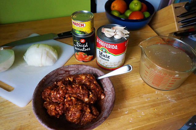 Ingredients: a large can of hominy, cans of tomatoes and chiles, and a bowl heaped with dark red-spiced chorizo