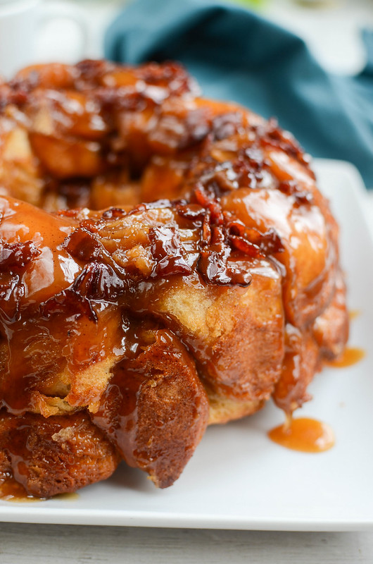 Monkey bread on a white plate, topped with bacon and with a dripping maple syrup sauce
