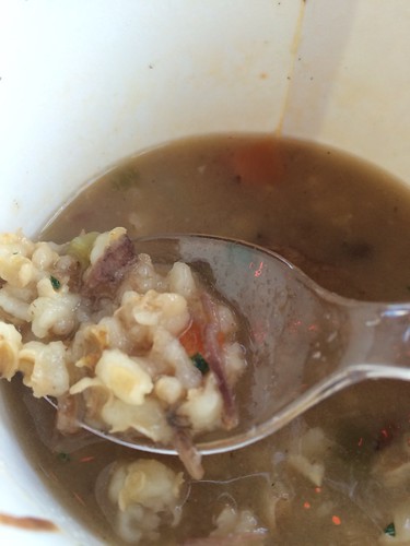 A spoonful of barley over a take-out cup of beef and barley soup.
