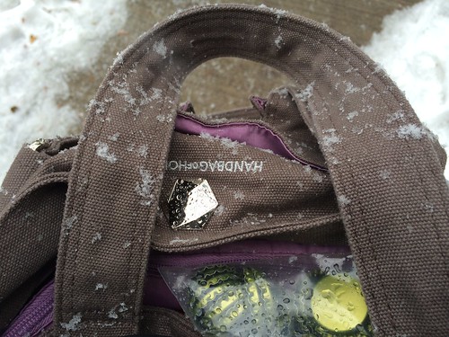 A close up of a handbag, lightly dusted in snow, containing a baggie of unused bottle caps.