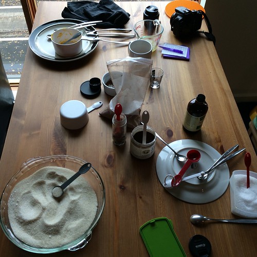A table covered in jars, plates, silverware, a camera, a notebook, and a variety of other things for intentional food experiments.