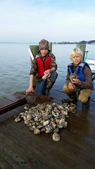Two kids on a pier looking at oysters.