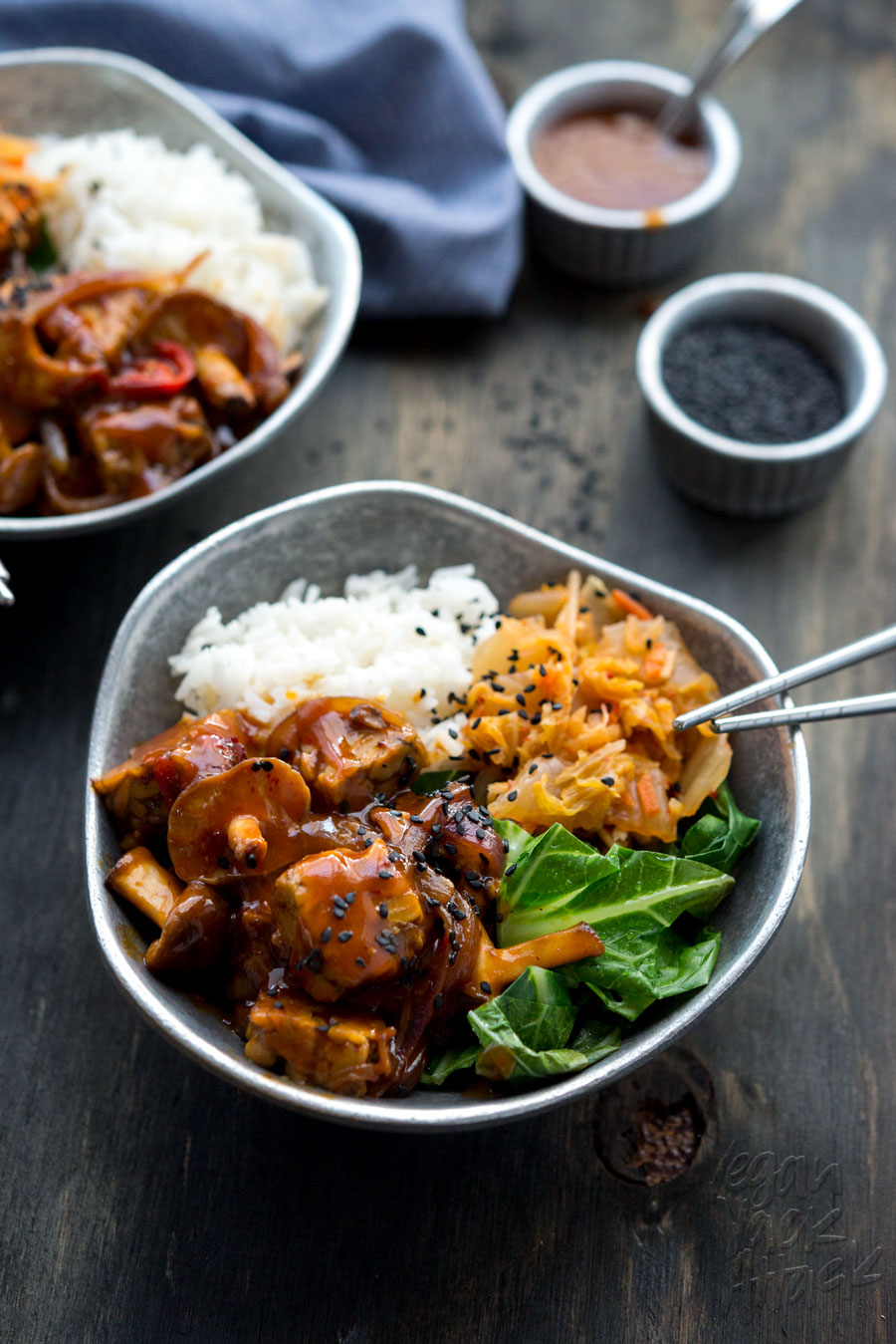 Bowl of Korean-style simmered tempeh with rice, kimchi, and greens on a black table