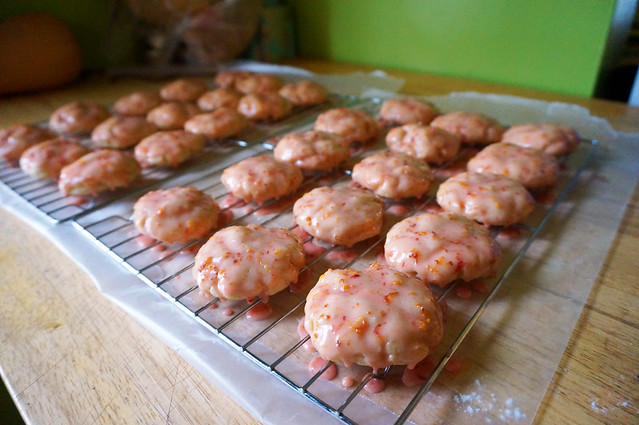 Two wire racks full of dipped cookies, small drops of pink glaze dripping on the wax paper below.