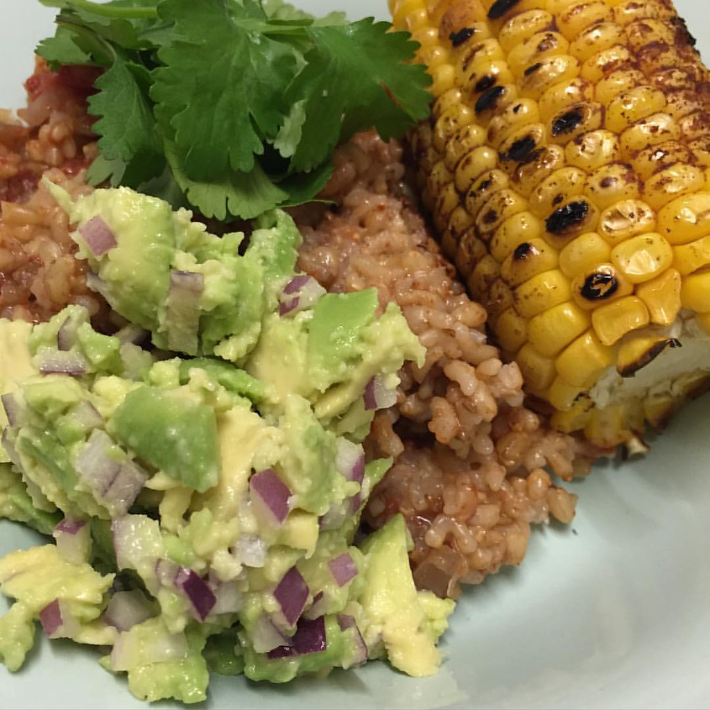 a plate full of mexican. mexican rice, guacamole and grilled corn on the cob