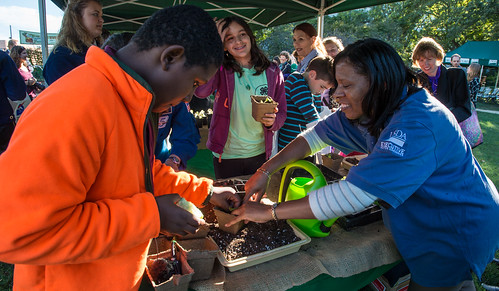 Jefferson Middle School student Troy Durham II, (in orange jacket) is assisted by a U.S. Department of Agriculture (USDA) Operations Program Specialist and Executive Master Gardner (blue shirt) while transplanting an “Outredgeous Red Romaine Lettuce” seedling grown from sister seeds to lettuce grown on the International Space Station, at an event in The People's Garden, at USDA's Whitten Building.