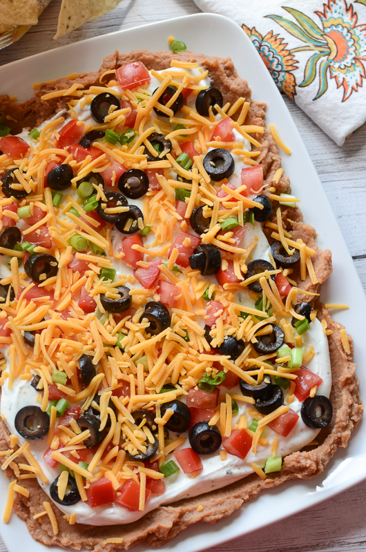 Layered Ranch Taco Dip - layered of refried beans, sour cream with ranch dressing mix, tomatoes, olive, green onions, and more! This is such a delicious dip recipe!