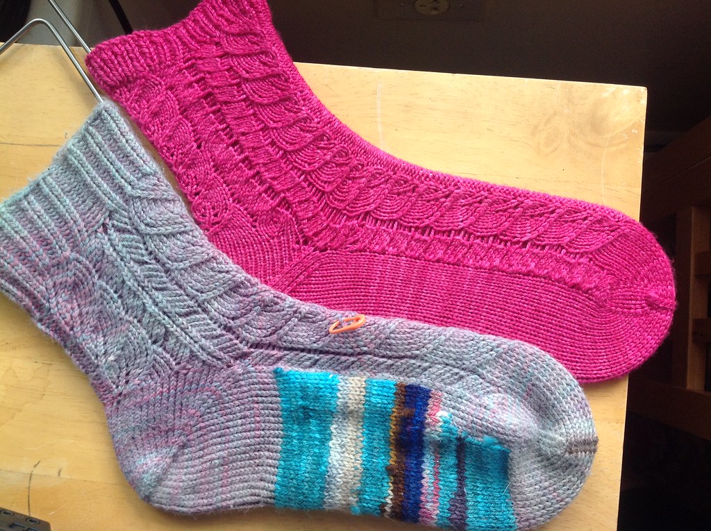 Two handknit socks, both the same pattern, one heavily worn and darned, the other new.