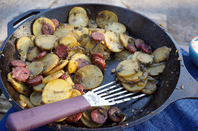 A black cast-iron pan of Mr. W's campout potatoes, a thin silver spatula resting among the discs of potato