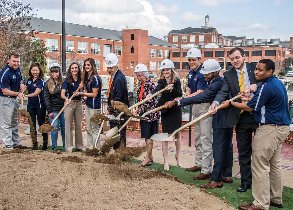 A group of people hold shovels with dirt during a groundbreaking ceremony.