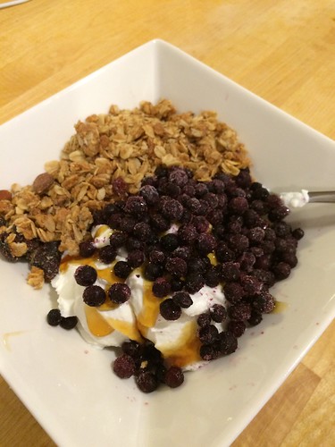 A square bowl full of Greek-style yogurt, frozen wild blueberries, granola, and honey. Also full of NOMNOMNOM.