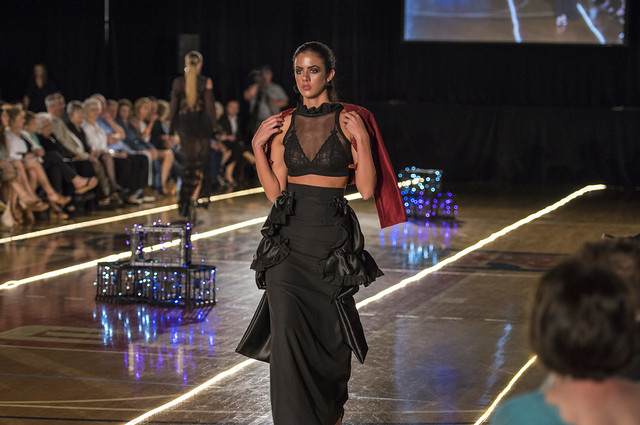 A student model in a 2-piece black dress walks down the runway