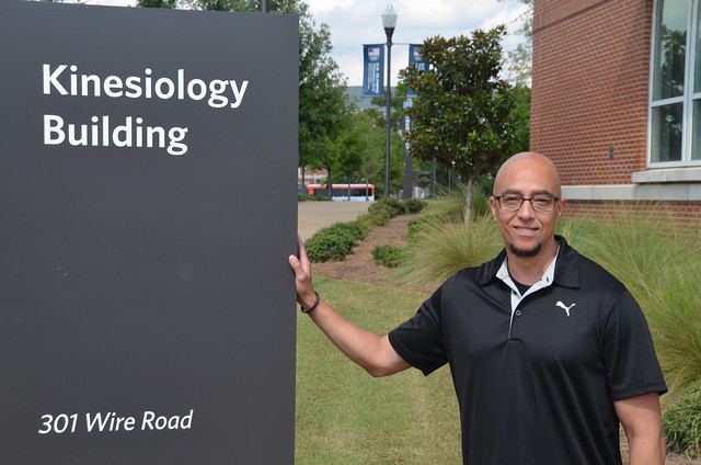 Professor Michael Brown stands next to a kinesiology building sign