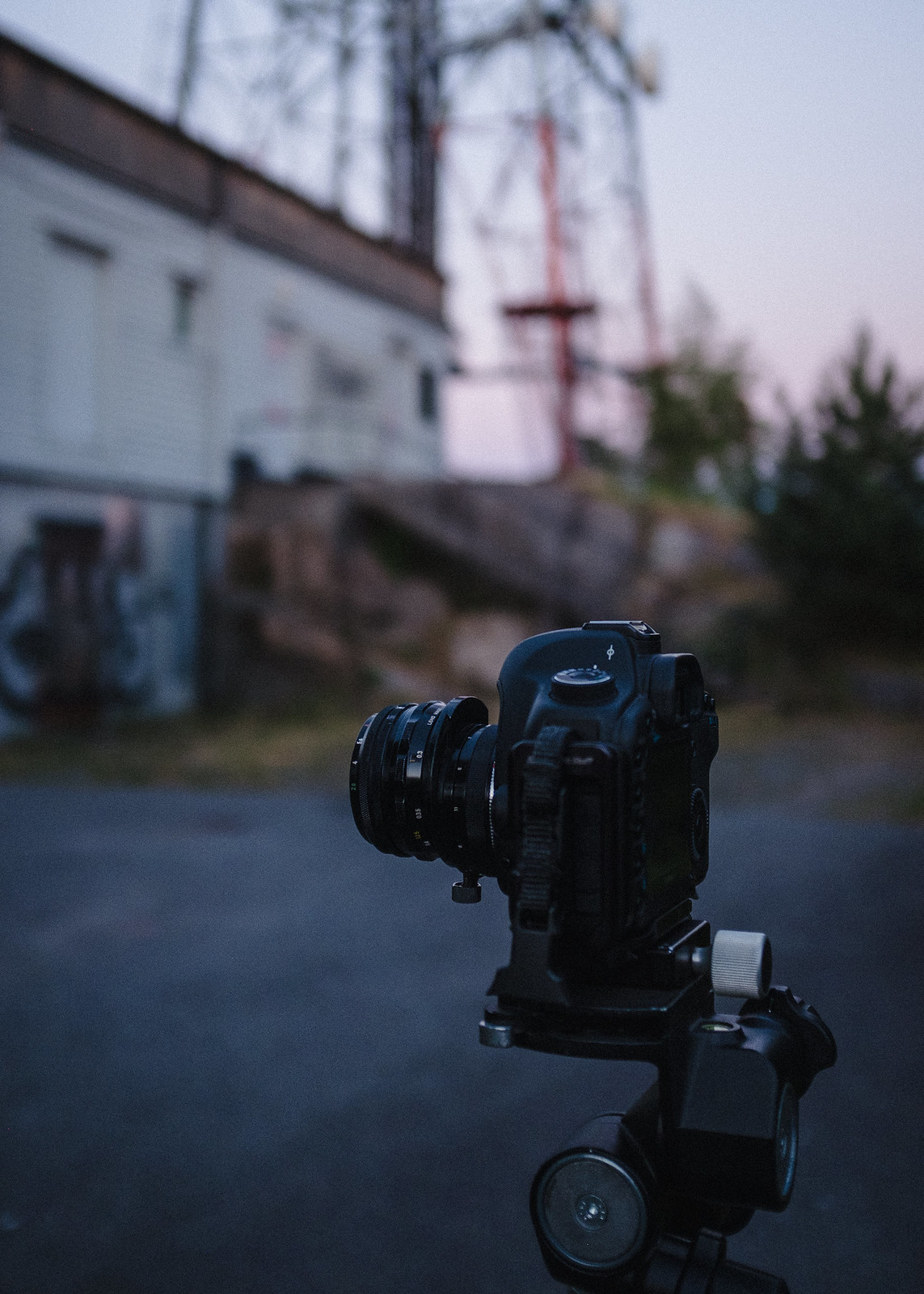 Camera on a tripod, some structures in the background.