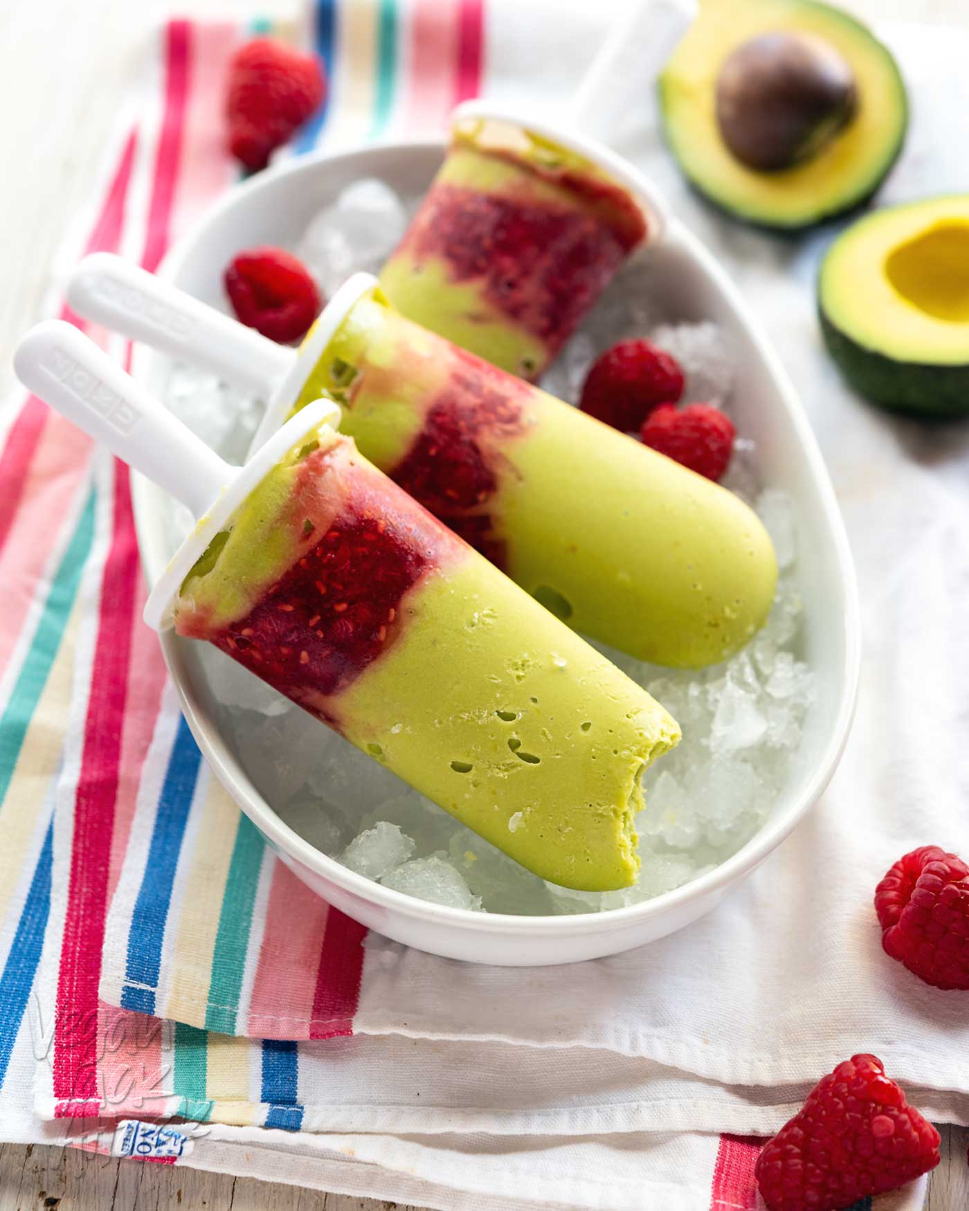 three avocado raspberry popsicles in a white, oval plate with crushed ice