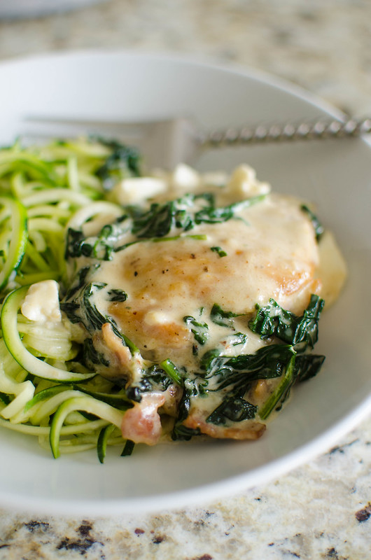 Chicken breast with spinach feta cream sauce on top of zucchini noodles on a white plate