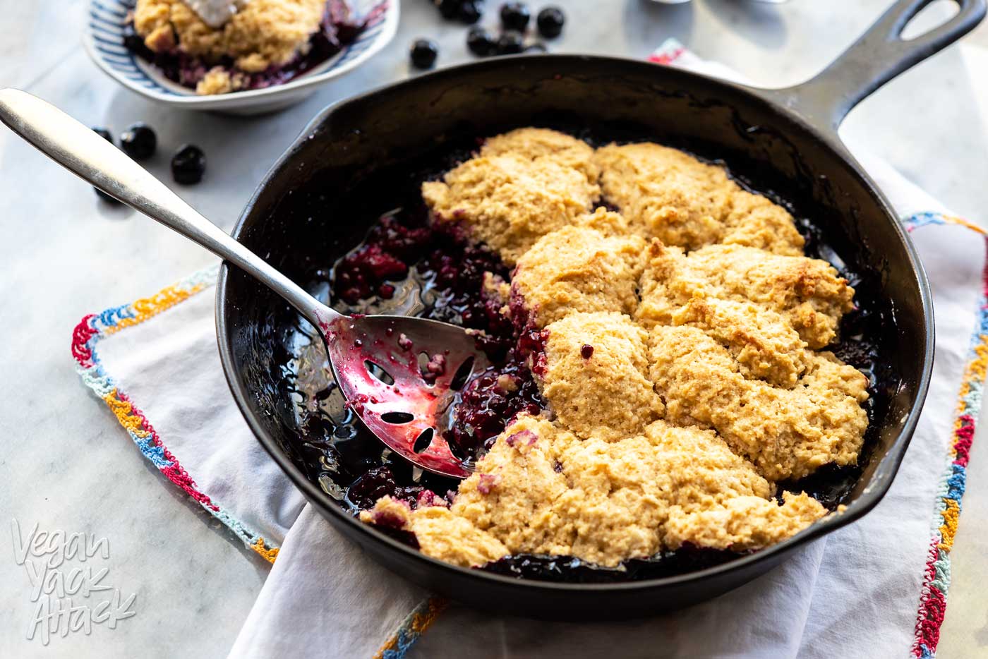 Cast iron skillet of blackberry cobbler with biscuit topping, with spoon