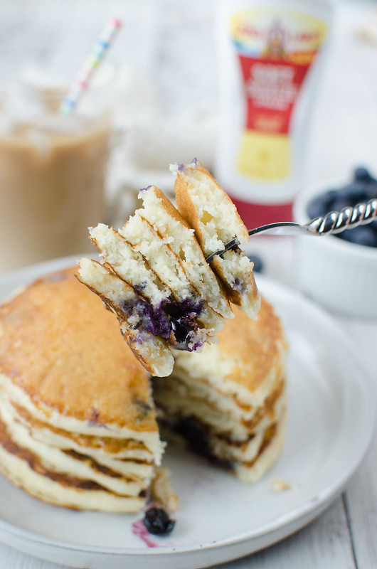 A stack of 5 blueberry pancakes with a fork holding a bite of each layer