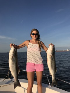 Photo of woman holding up two nice striped bass.