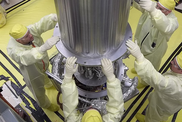 Four men in yellow lab suits surrounding the vacuum chamber during testing.
