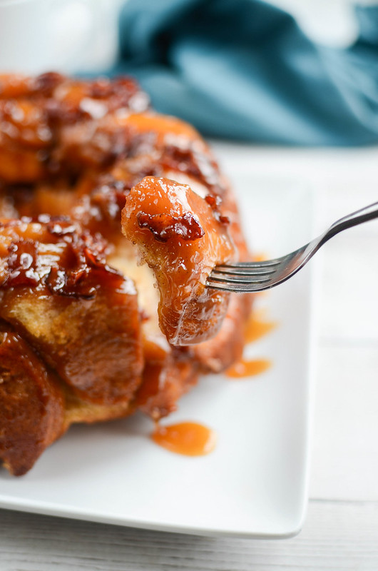 A fork holding a piece of monkey bread with the entire monkey bread in the background on a white plate