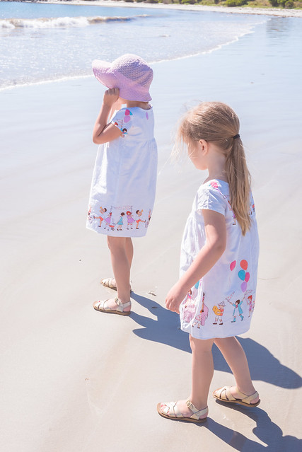 Two children at the beach. They wear matching dresses in Michael Miller "Children at Play" print.