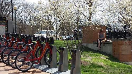 A woman eating lunch sits on a brick wall by the bike station, Silver Spring, Maryland, showing the value of places to sit in an area otherwise bereft of benches