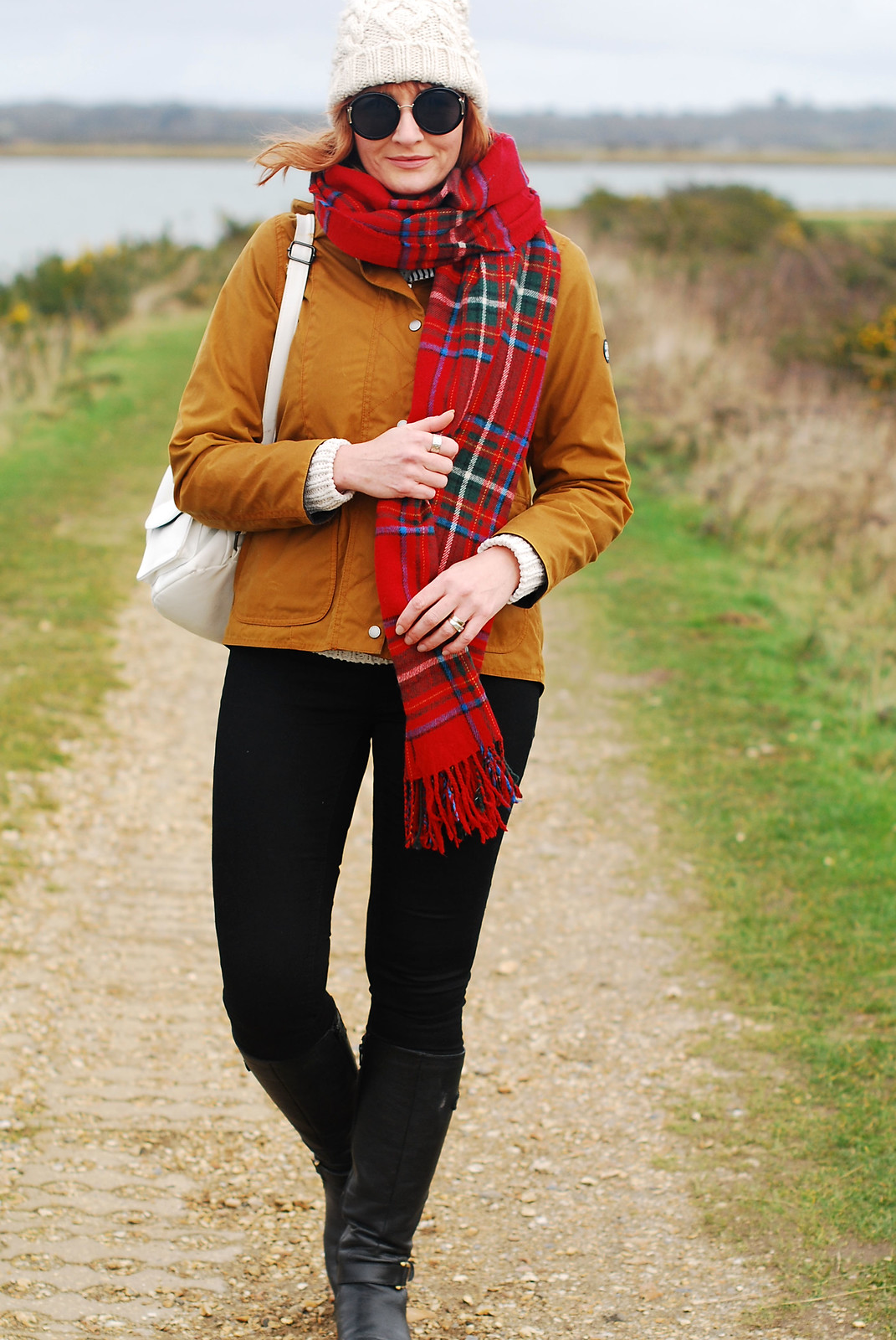 Cold weather preppy outfit for the coast: Brown Barbour jacket cream bobble hat and roll neck red tartan scarf black skinnies and riding boots | Not Dressed As Lamb, over 40 style blog