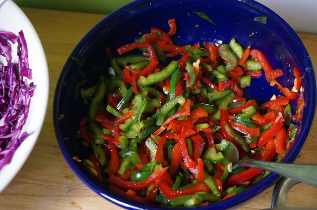 A serving bowl filled with lightly marinated peppers, brightly and temptingly red and green against the dark blue ceramic.