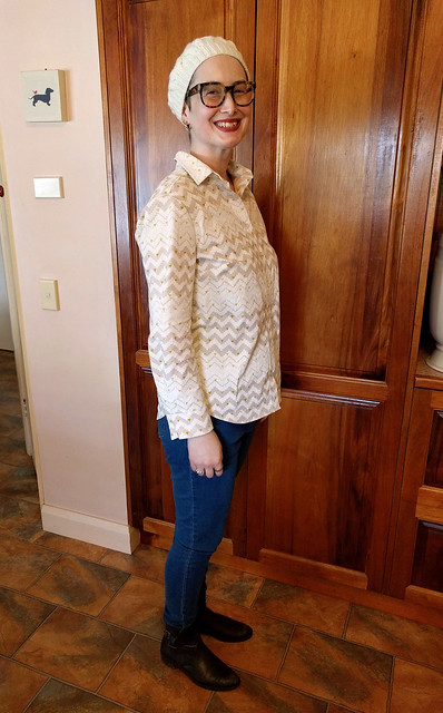 A woman wears a cream hand-knitted beret, geometric print button up shirt, skinny blue jeans and brown ankle boots.