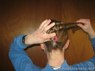 Place a finger to keep everything in place as you begin winding the braid around the hair elastic when making a Braided Bun - 12 Pretty & Practical Hiking Hairstyles