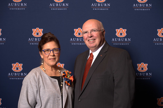 Barb Struempler and Timothy Boosinger pose for a photo in front of a navy blue Auburn University backdrop.