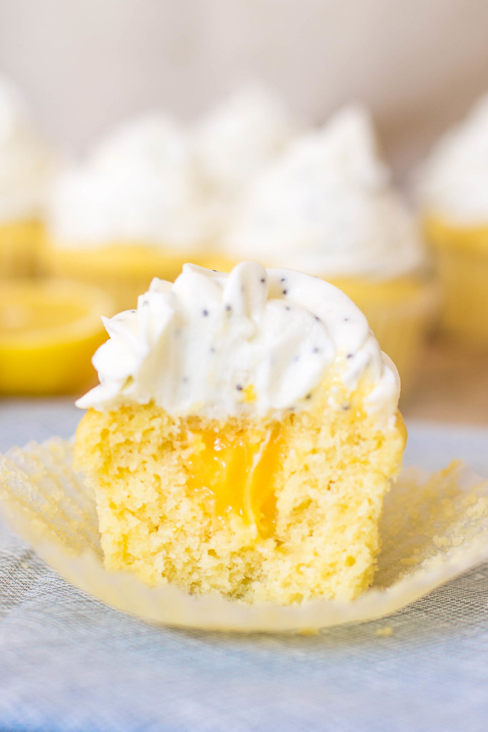 Perfect filled lemon cupcakes cut open to reveal lemon curd and a dome of cream cheese poppy seed frosting.