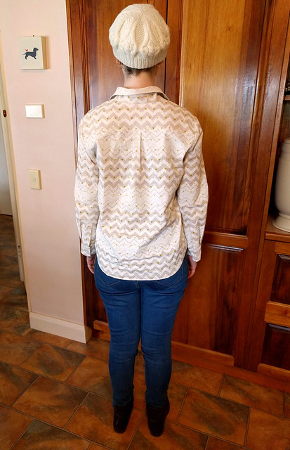 A woman wears a cream hand-knitted beret, geometric print button up shirt, skinny blue jeans and brown ankle boots.
