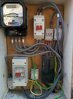 [Electricity distribution board with the live supply out of the 100A isolator going via the Power Meter]