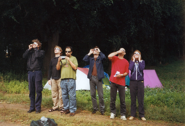 A photo from 1999 with six individuals in an outdoor setting in Reims, France (with tents behind them) safely viewing what presumably is a solar eclipse.