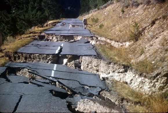 Image shows a blacktop road on a hillside, split open in several places where an earthquake has torn it to shreds.