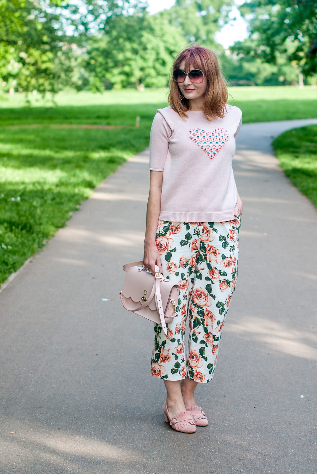 Blush pink summer outfit: Pink sweater with heart motif cropped floral trousers pants blush pink suede Gucci-style heeled loafers pink satchel | Not Dressed As Lamb, over 40 style