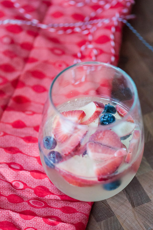 Make the 4th of July even more festive with this Red White and Blue Sangria. Strawberries, blueberries, peaches, white wine and sparkling lemonade all combine to create a delicious, refreshing drink that screams America.