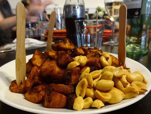 A small round white plate piled high with shelled peanuts and cubes of plantain fried to a deep brown.  Disposable wooden forks are stuck here and there in the mound of plantain.