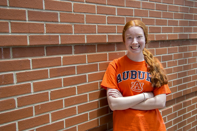 Carolina Williams wears an Auburn University T-shirt while posing for a photo against a brick wall.
