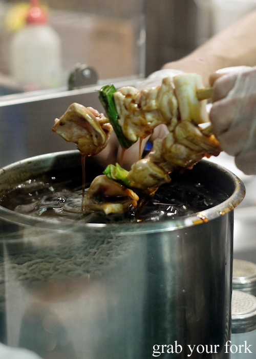 Dipping chicken skewers into tare yakitori sauce at Yakitori Jin Japanese restaurant in Haberfield Sydney