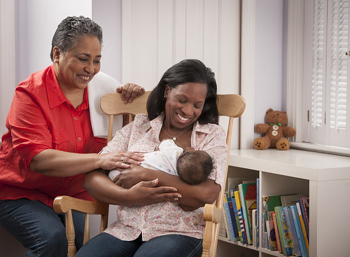 A woman breastfeeding in a chair with another woman beside her