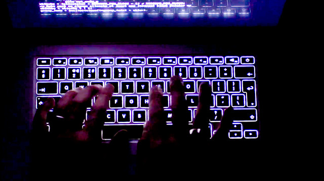 Two hands type on an illuminated keyboard.