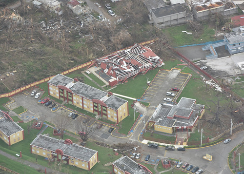 An aerial view of damage caused by Hurricane Maria. A huge building has had its roof shredded to ribbons.Other buildings have had bits ripped off. 